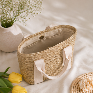 Woven basket with handles on a light surface with flowers and a vase.