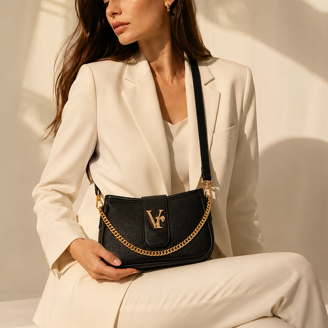 Woman holding a black handbag with gold chain strap against a neutral background