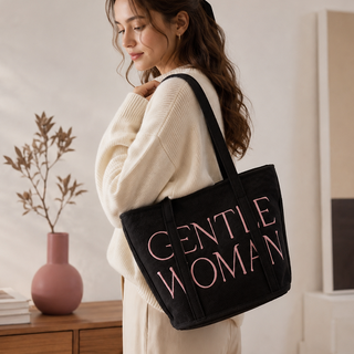 Woman holding a black tote bag with 'GENTLE WOMAN' text in a room setting.